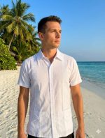 Eleva tu estilo veraniego con nuestra exclusiva guayabera de manga corta en blanco puro. Diseñada para el hombre moderno que busca frescura sin sacrificar la elegancia, esta prenda cuenta con exquisitos bordados verticales con patrones geométricos que resaltan su confección detallada. Sus bolsillos frontales y su corte relajado la convierten en la elección perfecta para bodas en la playa, eventos al atardecer o una escapada paradisíaca. Siente la brisa y luce impecable.